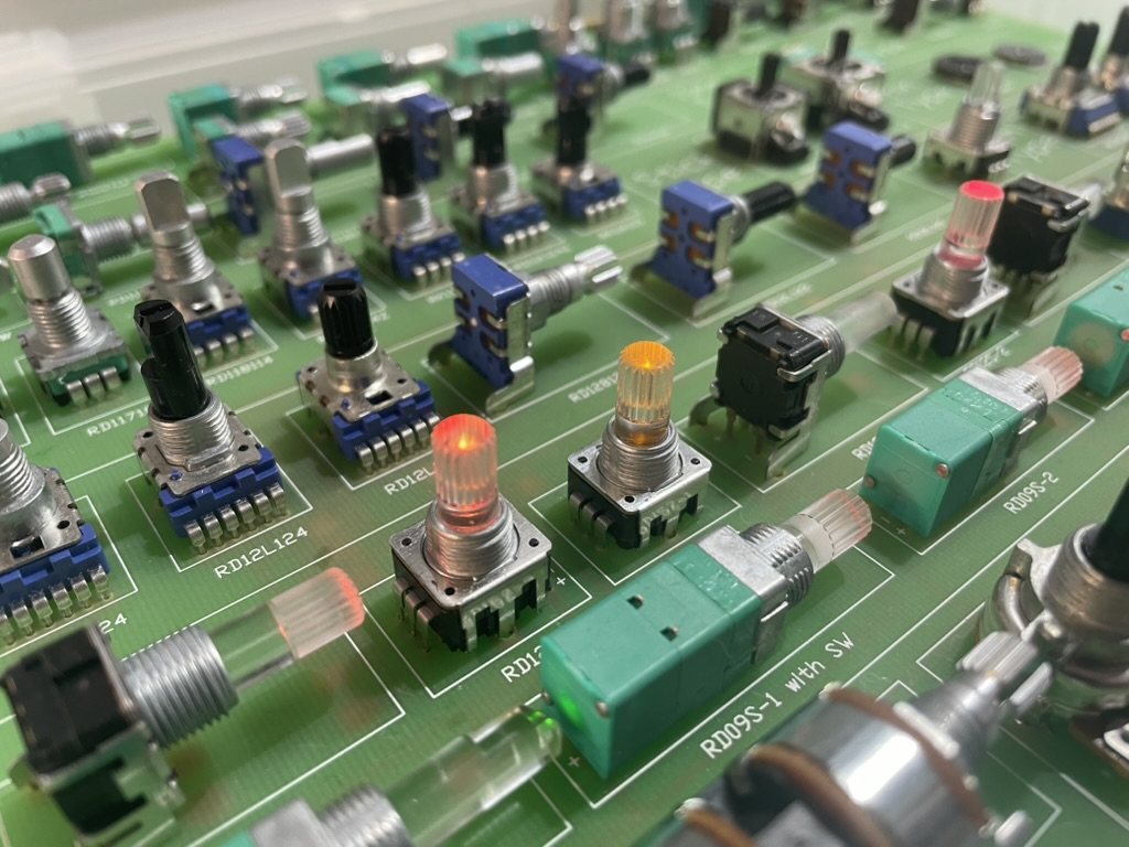 Close-up of rotary encoders, illuminated switches, and knobs on a hardware prototype board